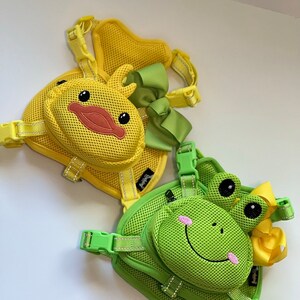 Puede incluir: Dos arneses para perros con un dise&ntilde;o de malla. Un arn&eacute;s es amarillo con un dise&ntilde;o de pato y un lazo verde. El otro arn&eacute;s es verde con un dise&ntilde;o de rana y un lazo amarillo.