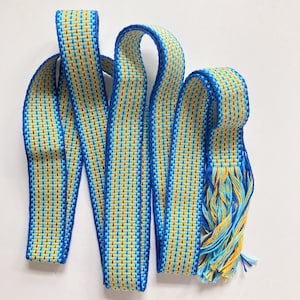 May include: Blue and yellow woven ribbon with fringe ends. The ribbon is made of a thin, textured material and has a repeating pattern of blue and yellow stripes.