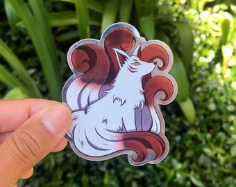 May include: A silver holographic sticker featuring a white fox with red and brown fur. The fox has nine tails, each with a swirl design. The sticker is perfect for adding a touch of whimsy to laptops, water bottles, or journals.