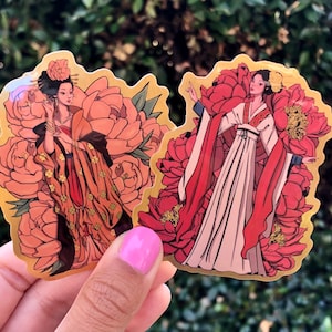 May include: Two gold foil stickers featuring women in traditional Asian clothing with floral patterns. The women are surrounded by pink and red peonies.