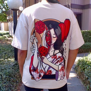 Op de afbeelding: Wit T-shirt met een grafische print van een vrouw met een rode en witte waaier en een rode lantaarn. Het gezicht van de vrouw is half mens en half demon.