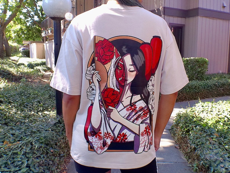 Op de afbeelding: Wit T-shirt met een grafische print van een vrouw met een rode en witte waaier en een rode lantaarn. Het gezicht van de vrouw is half mens en half demon.