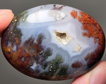 Puede incluir: Una piedra de ágata pulida con un patrón de bandas blancas, azules, verdes y marrones. La piedra tiene un agujero natural en el centro.