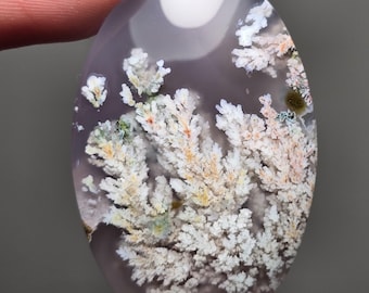May include: A polished agate cabochon with a dendritic pattern. The agate is a light purple color with white, pink, and green dendrites.