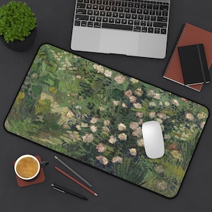 May include: Rectangular desk mat featuring a floral painting with green and white hues. The mat has a black border and is surrounded by a laptop, mouse, pens, a coffee cup, and notebooks. The artwork resembles a garden scene.