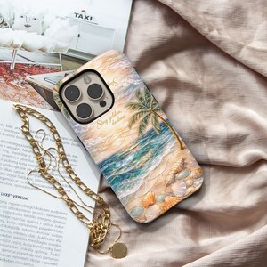 May include: A phone case featuring a beach scene with a palm tree, ocean waves, and seashells. The case has the words "Stay golden, darling" in script. The case is tan, blue, and gold.