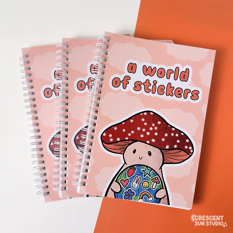 Spiral bound book with a background of peachy clouds. Coral text reads "a world of stickers." Below that is a happy mushroom holding a globe covered in stickers.