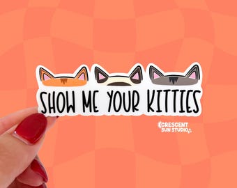 Può includere: Un adesivo rettangolare bianco con tre orecchie di gatto illustrate in arancione, crema e grigio, con il testo nero SHOW ME YOUR KITTIES e il piccolo testo bianco CRESCENT SUN STUDIO stampato sotto il lato destro della scritta.