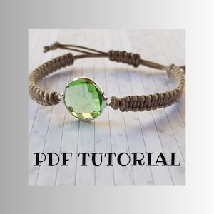 Op de afbeelding: Een bruin koordarmband met een groene edelsteen in het midden. De armband is aan beide kanten van de edelsteen met een knoop vastgemaakt. De afbeelding bevat de tekst "PDF TUTORIAL".