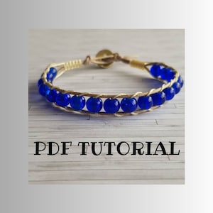Puede incluir: Un brazalete azul y beige con un cierre dorado. El brazalete está hecho con cuentas de vidrio azul y cordón beige. La imagen incluye el texto "PDF TUTORIAL".