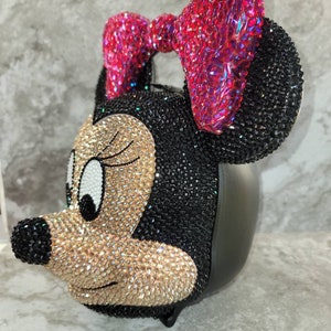 Puede incluir: Un bolso de Minnie Mouse cubierto de pedrer&iacute;a negra y dorada con un lazo rosa.