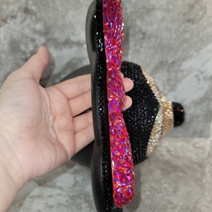 Puede incluir: Una diadema negra y roja adornada con joyas, con una gran joya roja brillante en el lateral. La diadema est&aacute; hecha de un material flexible y est&aacute; adornada con peque&ntilde;as joyas negras.