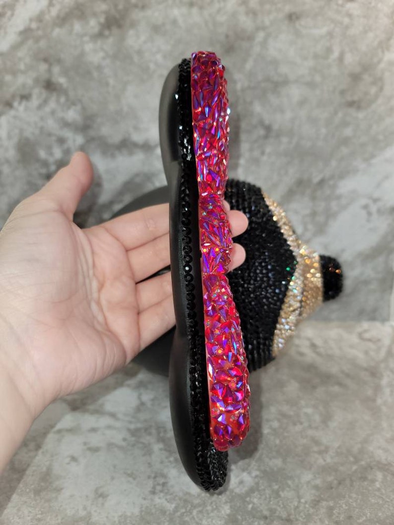 Puede incluir: Una diadema negra y roja adornada con joyas, con una gran joya roja brillante en el lateral. La diadema est&aacute; hecha de un material flexible y est&aacute; adornada con peque&ntilde;as joyas negras.