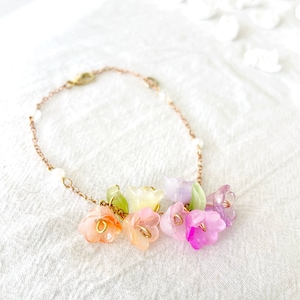 Puede incluir: Un delicado brazalete de cadena dorada con un grupo de abalorios de flores en colores pastel. Los abalorios son de vidrio y están en tonos de rosa, morado, verde y amarillo.