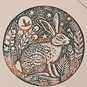 以下が含まれることがあります： 葉、星、三日月の中の鳥に囲まれたウサギの詳細なイラストが描かれた円形のプリント。 アートワークは、ティール、ブラウン、白の色合いを使用し、素朴で自然にインスパイアされた美学を作り出しています。