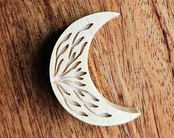 Può includere: Ritaglio di legno a forma di mezzaluna con un disegno floreale intagliato sulla sua superficie. La luna è di colore chiaro e i dettagli intagliati creano un'ombra contrastante. Lo sfondo con venature del legno aggiunge un'estetica naturale.