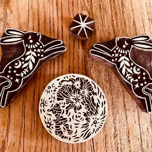 May include: A selection of wooden block stamps with detailed patterns. Two stamps depict a rabbit silhouette with floral and celestial motifs. A circular stamp showcases a floral design, and a small starburst stamp is included.