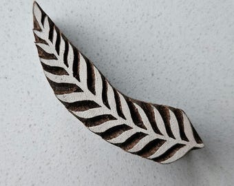 May include: A wooden leaf-shaped stamp with a detailed white leaf pattern on a brown background. The stamp is curved and appears to be hand-carved, suitable for textile printing or crafting projects.