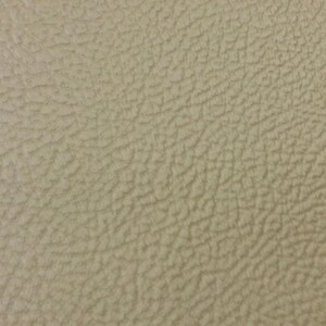 K&ouml;nnte beinhalten: Nahaufnahme eines strukturierten, beigefarbenen Ledermaterials. Die Oberfl&auml;che hat ein leicht raues, narbiges Aussehen mit subtilen Farbvariationen. Der Gesamteffekt ist ein neutraler, nat&uuml;rlicher Look.
