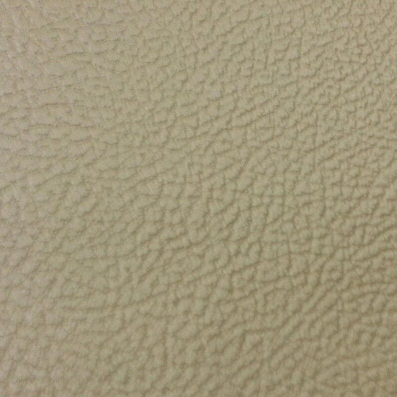 K&ouml;nnte beinhalten: Nahaufnahme eines strukturierten, beigefarbenen Ledermaterials. Die Oberfl&auml;che hat ein leicht raues, narbiges Aussehen mit subtilen Farbvariationen. Der Gesamteffekt ist ein neutraler, nat&uuml;rlicher Look.
