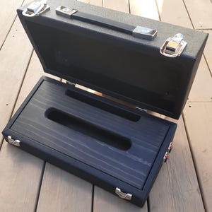 May include: Black pedalboard case with a wood interior and two red jacks on the side. The case is open and the lid is propped up.