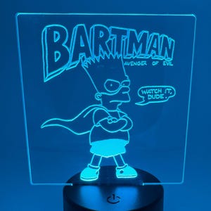 May include: A blue LED night light featuring Bart Simpson as "Bartman". The light has the words "BARTMAN AVENGER OF EVIL" and "WATCH IT, DUDE." The light is on a black base.