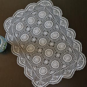 Könnte beinhalten: Weiße Häkeldeckchen mit einem runden Muster. Die Deckchen haben einen gewellten Rand und sind aus zarter Spitze gefertigt.