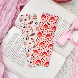 May include: Two bookmarks with different patterns. One bookmark features a pink background with a repeating pattern of teacups, butterflies, and flowers. The other bookmark features a pink background with a repeating pattern of red foxes wearing hats and leaves.