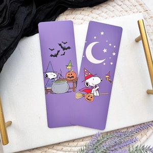 May include: Two purple Halloween themed bookmarks featuring Snoopy dressed as a witch. One bookmark shows Snoopy stirring a cauldron with Woodstock, the other shows Snoopy flying on a broomstick.