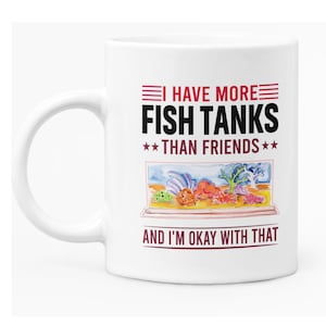 May include: White ceramic coffee mug with a black and red design. The mug reads "I have more fish tanks than friends and I'm okay with that". The design includes a cartoon image of a fish tank with colourful fish and coral.