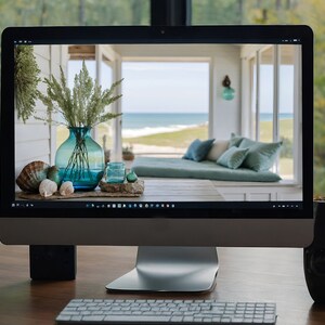 Puede incluir: Un monitor de computadora que muestra una foto del interior de una casa de playa con un sof&aacute; y una ventana con vista al oc&eacute;ano. La foto est&aacute; decorada con un jarr&oacute;n de flores secas y conchas marinas sobre una mesa.