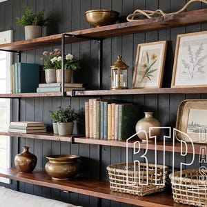 Op de afbeelding: Houten planken met diverse decoratieve items. Inclusief ingelijste botanische prints, lantaarns, boeken, vazen en potplanten. De planken staan tegen een donkergrijze muur, wat een gezellige, rustieke uitstraling creëert.