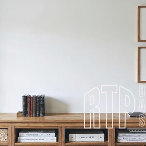 Puede incluir: Un mueble de madera con cestas tejidas y estantes, que contiene libros y cajas. Dos impresiones de paisajes en blanco y negro enmarcadas cuelgan encima. El texto "RTD DIGITAL ART STUDIO" está superpuesto.