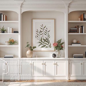 May include: A white, built-in bookcase with shelves displaying books, ornaments, and plants. A framed botanical print is centrally placed. The lower cabinets have gold handles. The text "DIGITAL ART STUDIO" is visible.