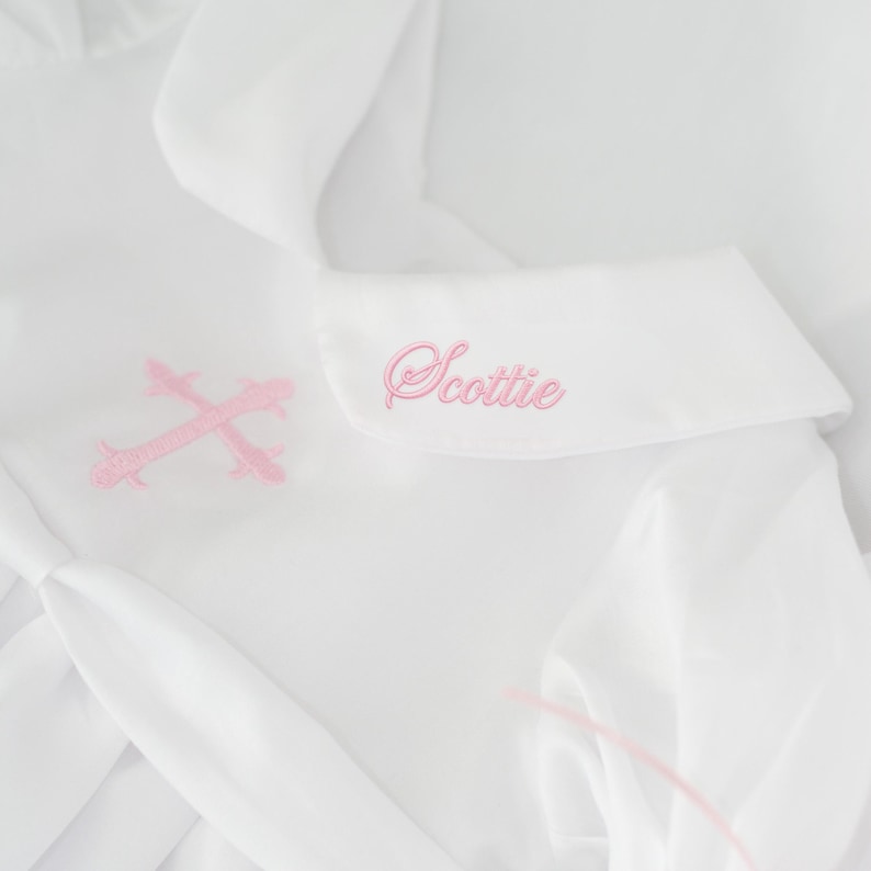 Close-up of soft pink cross embroidery and monogram stitched on collar.