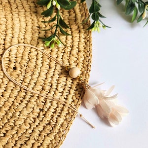 May include: A delicate, light pink tassel with a wooden bead and gold accents hangs from a woven straw mat. The tassel is made of soft, feathery material.