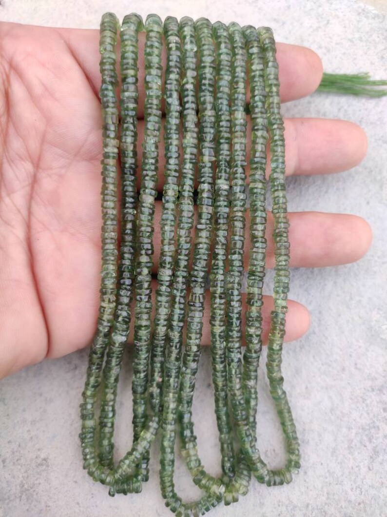 May include: A strand of green gemstone beads, likely aventurine, with a faceted, cylindrical shape. The beads are strung on a clear thread and are approximately 4mm in diameter.
