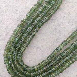 May include: A strand of green gemstone beads, with a faceted, slightly rounded shape. The beads are strung on a clear thread and are arranged in a loose, flowing pattern.