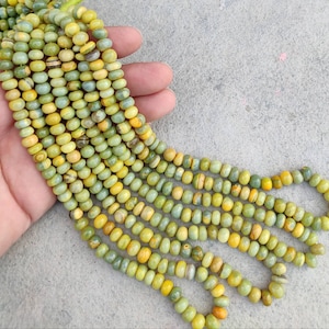 May include: A strand of green and yellow gemstone beads. The beads are round and have a smooth, polished finish. The beads are strung on a clear thread.