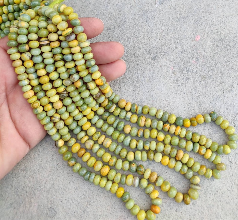 May include: A strand of green and yellow gemstone beads. The beads are round and have a smooth, polished finish. The beads are strung on a clear thread.