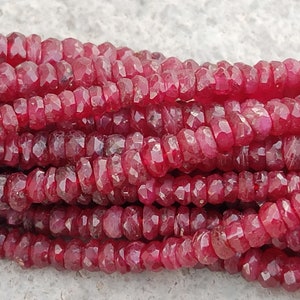 May include: A strand of deep red ruby beads, each bead is faceted and has a slightly irregular shape. The beads are strung together on a clear thread.