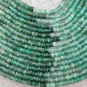 Puede incluir: Primer plano de múltiples hilos de cuentas de piedras preciosas verdes. Las cuentas varían en tonalidad de verde claro a oscuro, con algunas cuentas negras intercaladas. Las cuentas son pequeñas y redondas, ensartadas para formar collares o pulseras.