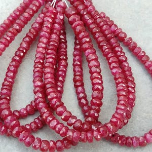 May include: Multiple strands of faceted, deep red ruby beads arranged in loops. Each bead features a small, circular, disc-like shape with a reflective, multi-faceted surface that catches the light, creating a consistent, vibrant crimson appearance.