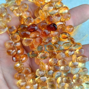 Könnte beinhalten: Eine Strähne aus goldgelben Edelsteinperlen mit facettierter ovaler Form. Die Perlen sind auf einem durchsichtigen Faden aufgefädelt und haben einen Durchmesser von etwa 8 mm.