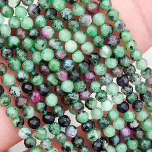 Peut inclure: Un brin de perles de pierres précieuses vertes, noires et roses. Les perles sont facettées et présentent une variété de motifs.