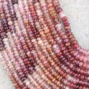 Puede incluir: Primer plano de múltiples hebras de cuentas de piedras preciosas en tonos rosa, rojo y naranja. Las cuentas son pequeñas e irregulares, creando una superficie texturizada. La paleta de colores varía del rosa claro al burdeos oscuro.