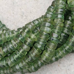May include: A strand of green glass beads, each bead is faceted and has a slightly rounded shape. The beads are strung together in a continuous loop.
