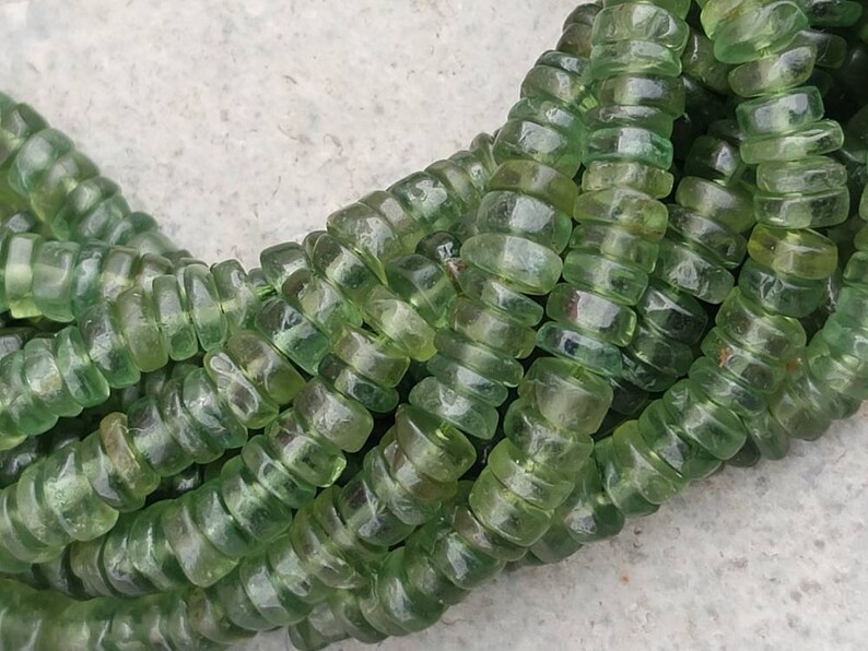 May include: A strand of green glass beads, each bead is faceted and has a slightly rounded shape. The beads are strung together in a continuous loop.
