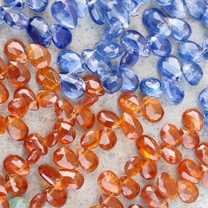 May include: A close-up of two strands of gemstone beads. One strand is made of orange-brown faceted beads, and the other strand is made of blue faceted beads.