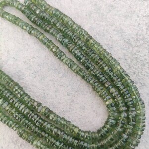 May include: A strand of green gemstone beads, with a faceted, round shape. The beads are strung on a clear thread and are arranged in a long, continuous line.